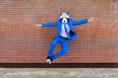 Full length of man jumping against brick wall
