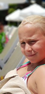 Close-up portrait of smiling girl sitting on deck chair at beach during sunny day