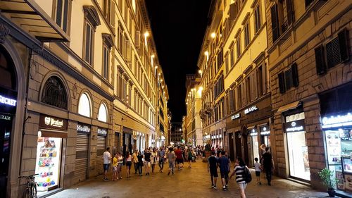 People on illuminated street amidst buildings at night