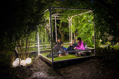 Children sitting on wooden structure by trees