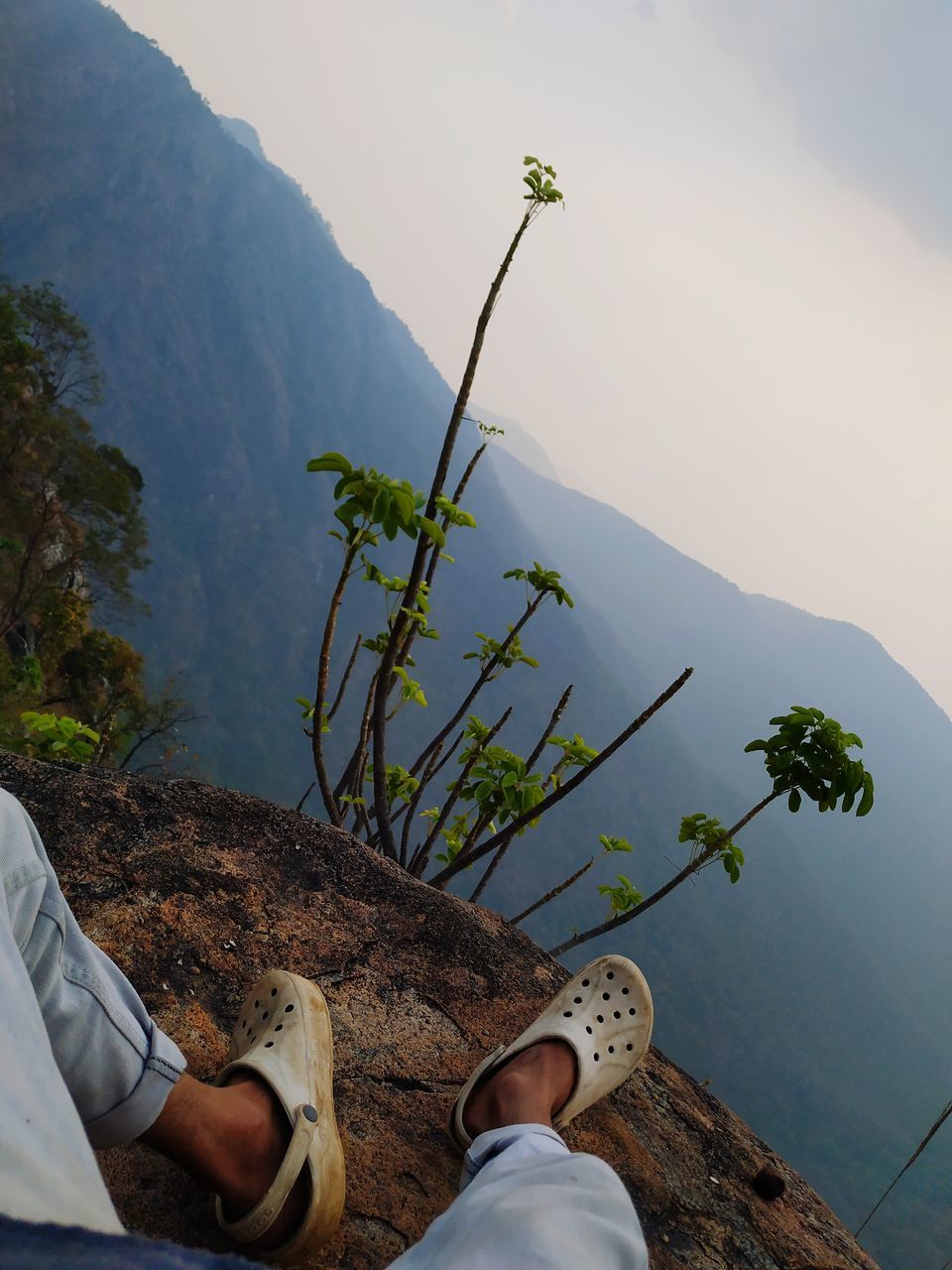 one person, nature, human leg, plant, low section, leisure activity, water, mountain, shoe, personal perspective, beauty in nature, adult, lifestyles, relaxation, men, scenics - nature, limb, sky, day, human limb, tree, outdoors, environment, land, lake, human foot, tranquility, holiday, vacation, trip, mountain range, travel, sitting, footwear, landscape, casual clothing, activity, high angle view, travel destinations, tranquil scene, flower