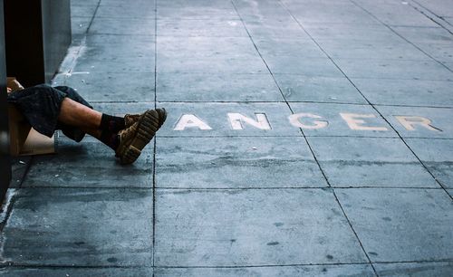 Low section of homeless man sitting by wall on street