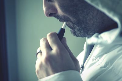 Midsection of mid adult man smoking while standing against wall