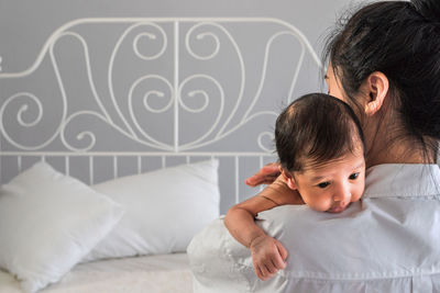 Close-up of woman holding newborn son on bed at home