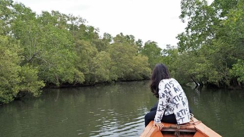 Rear view of woman sitting on riverbank against sky