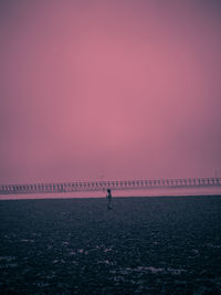 Distant view of boy standing at beach against clear sky during sunset