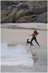Rear view of woman playing with dog at beach