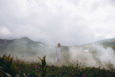 Woman standing on pink flowering plants against sky