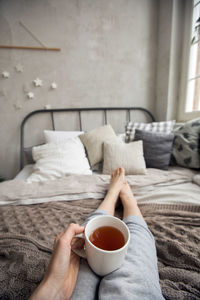 From above shot of anonymous barefoot female enjoying tea while sitting on comfortable bed 