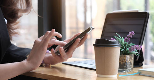 Midsection of woman holding mobile phone on table