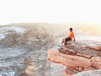 Rear view of woman sitting on rock against sky