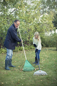 Grandfather and granddaughter raking autumn leaves at yard