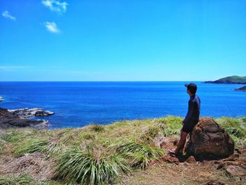 Rear view of woman standing by sea against clear blue sky