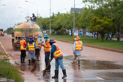 Rear view of sweepers cleaning road against sky