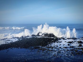 Waves splashing on shore against blue sky