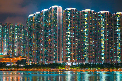 River by modern buildings against sky at night