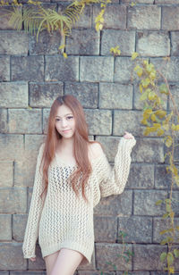 Portrait of sensuous young woman standing against stone wall