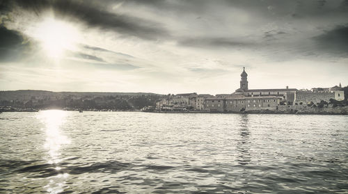 Buildings at waterfront against cloudy sky