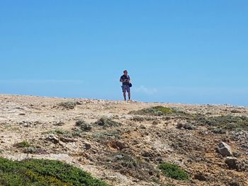 Rear view of woman standing on rock by sea against clear sky