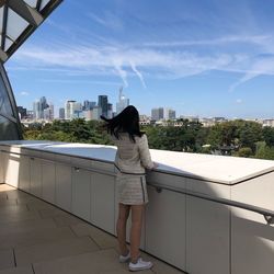 Rear view of woman standing in city against blue sky