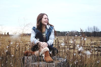 Young woman sitting on field against bare trees