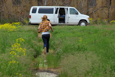 Rear view of girl running on field against car