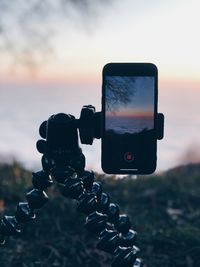 Close-up of camera photographing against sky during sunset