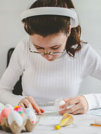 Teenage girl in a turtleneck, headphones and glasses holds a bunny egg and peels of off a sticker