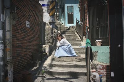 Portrait of young woman sitting on steps amidst houses in city