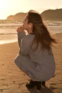 Young woman sitting on shore at beach during sunset