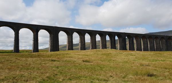 Arch bridge on field against sky