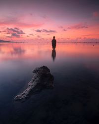 Man standing on rock by sea against sky during sunset