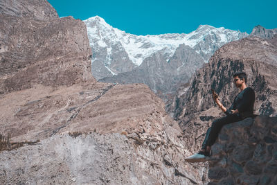 Full length of man sitting on rock against mountains