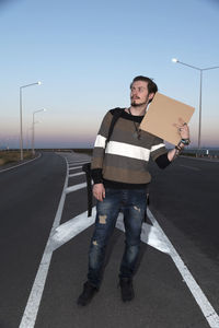 Man with cardboard standing on road against sky