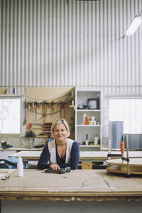 Portrait of smiling female carpenter leaning on workbench