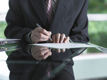 Midsection of businessman writing on document at desk