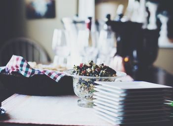 Food in bowl by stacked plates on table