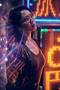 Woman looking away while standing at night next to neon sign in tokyo