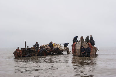 People on boats in sea against sky