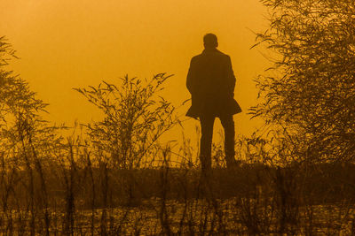 Silhouette man standing on field against orange sky