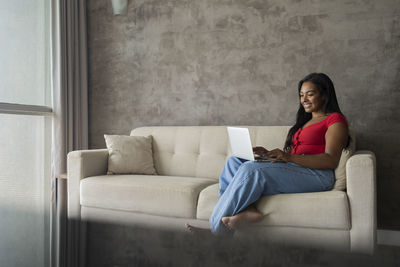 Young black woman working at home with laptop on her lap sitting on her couch  notebook for working. 