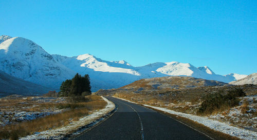 Road amidst snowcapped mountains against clear sky