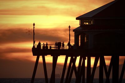 Silhouette people on pier over sea against sky during sunset