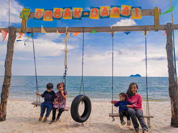 Siblings sitting on swings at beach