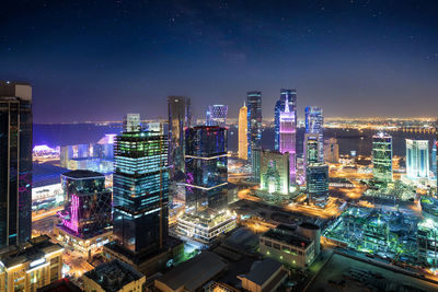 Illuminated modern buildings in city against sky at night