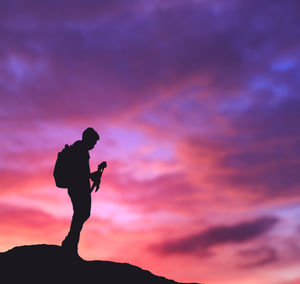 Silhouette man standing on rock against sky during sunset