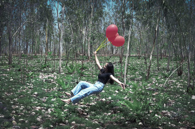 Rear view of woman with balloons against trees in forest