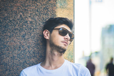 Close-up of young man wearing sunglasses standing against wall