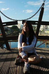 Full length of thoughtful young woman sitting on bridge in city