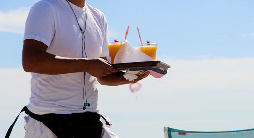 Midsection of waiter carrying drinks in tray against sky on sunny day